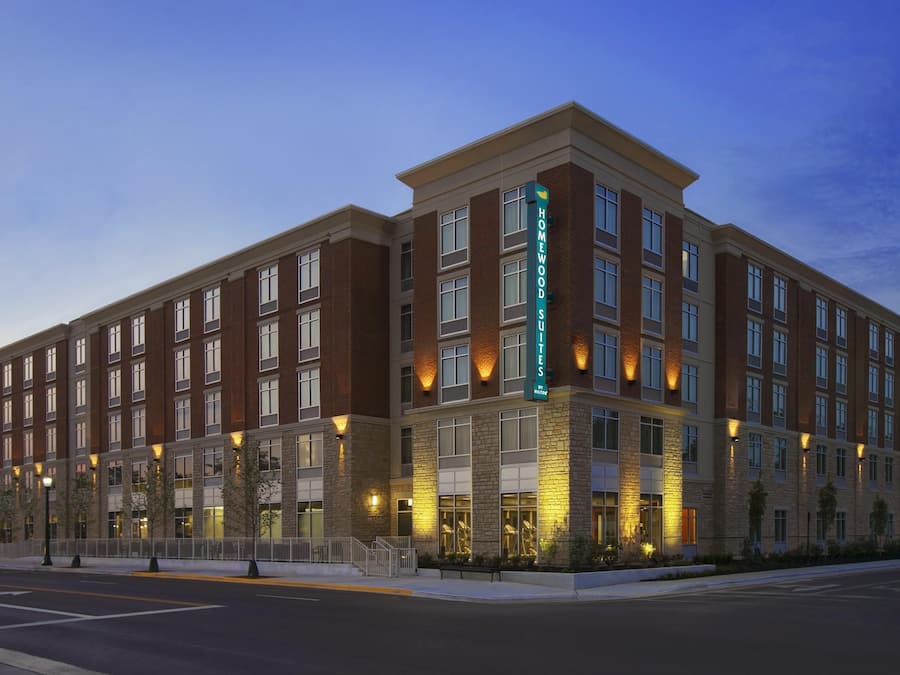 A multi-story hotel with a brick facade, large windows, and a prominent sign indicating it is a Homewood Suites.
