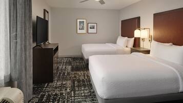 A hotel room with two beds, a flat-screen TV, a ceiling fan, and a wall-mounted light fixture.