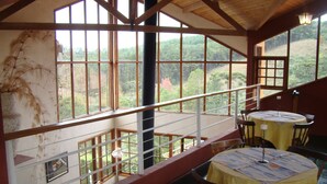Una habitación con ventanas amplias que ofrecen vistas a un paisaje boscoso. Hay una mesa con sillas dispuestas para comer.