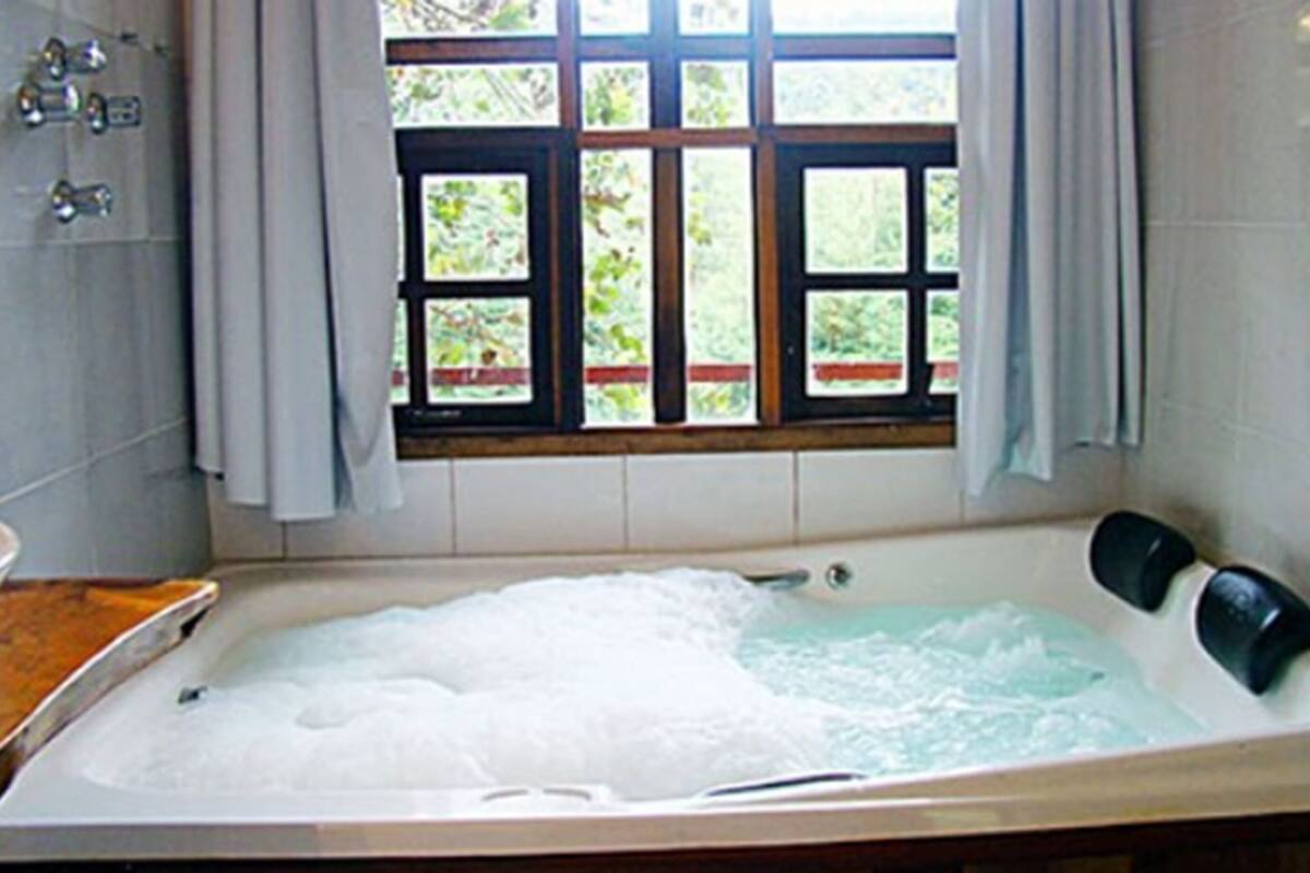Un baño con una bañera llena de agua, una ventana con vistas a zonas verdes y un mostrador de madera.