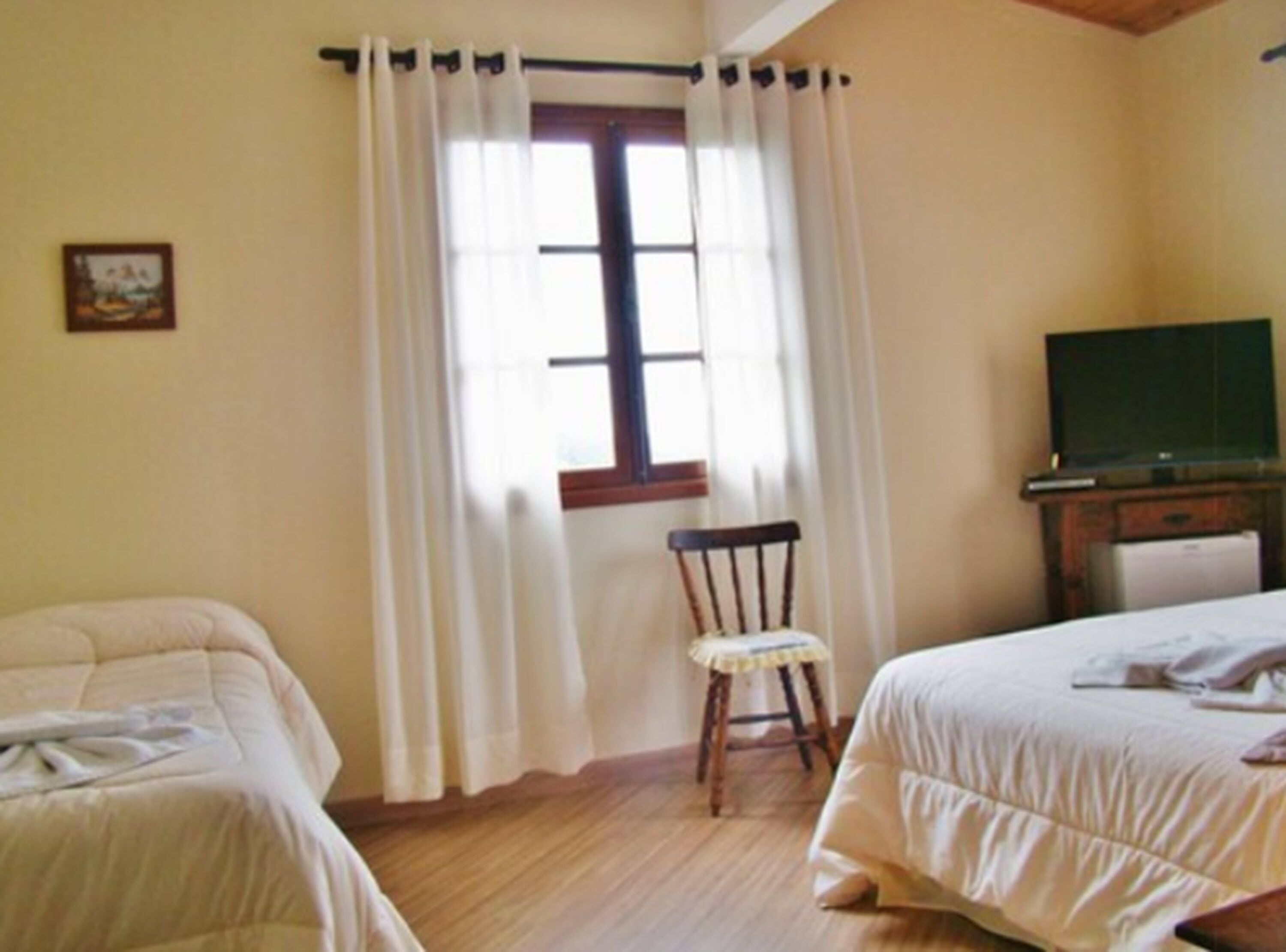 A bedroom with two beds, a wooden chair, a television, and a window with curtains.