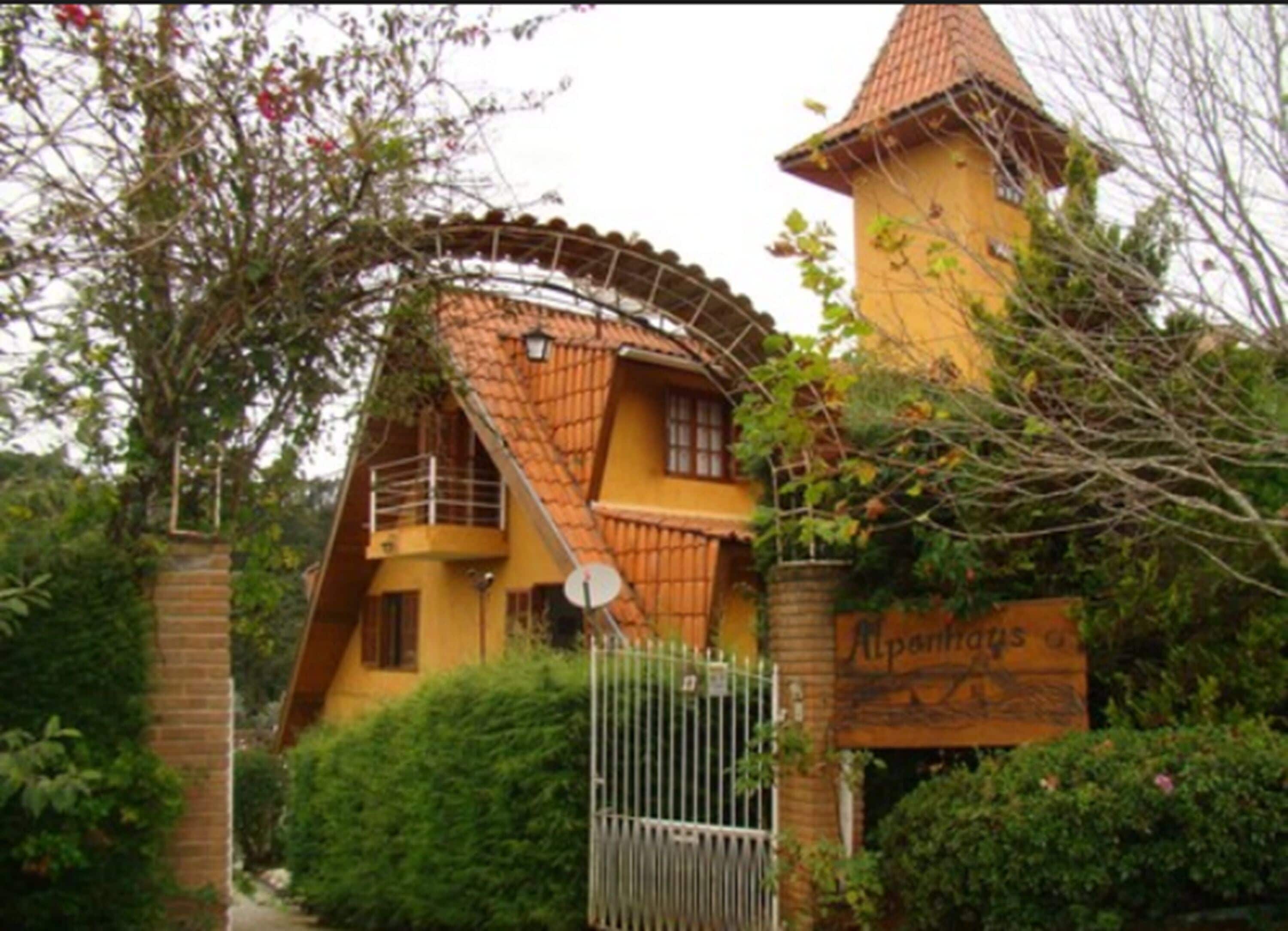 Un edificio con techo curvo y una pequeña torre, rodeado de vegetación y una reja de metal.