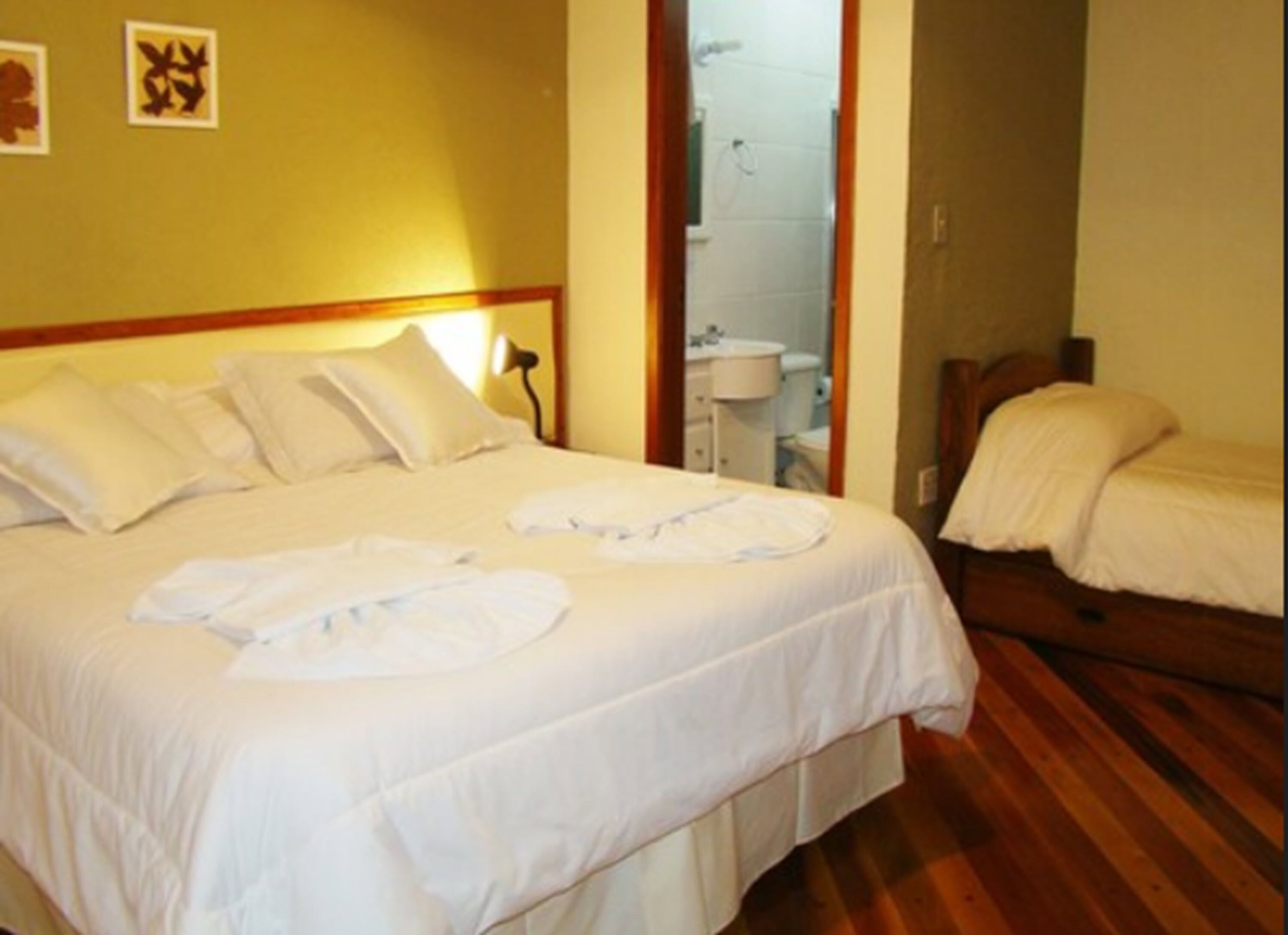 Habitación de hotel con una cama grande, una cama más pequeña, un baño visible a través de una puerta abierta y piso de madera.
