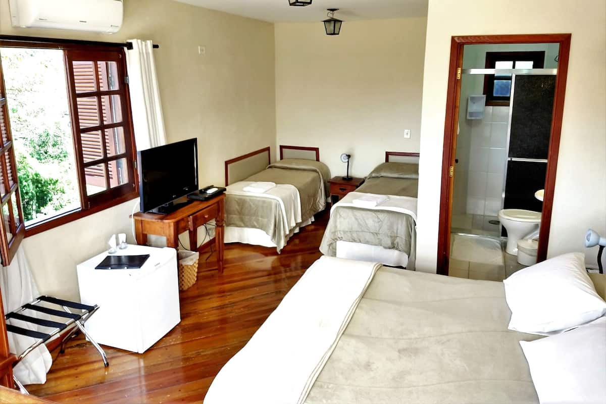 Una habitación de hotel con una cama, dos mesitas de noche, un televisor, una pequeña mesa con una silla, una ventana con contraventanas y una puerta que da al baño.