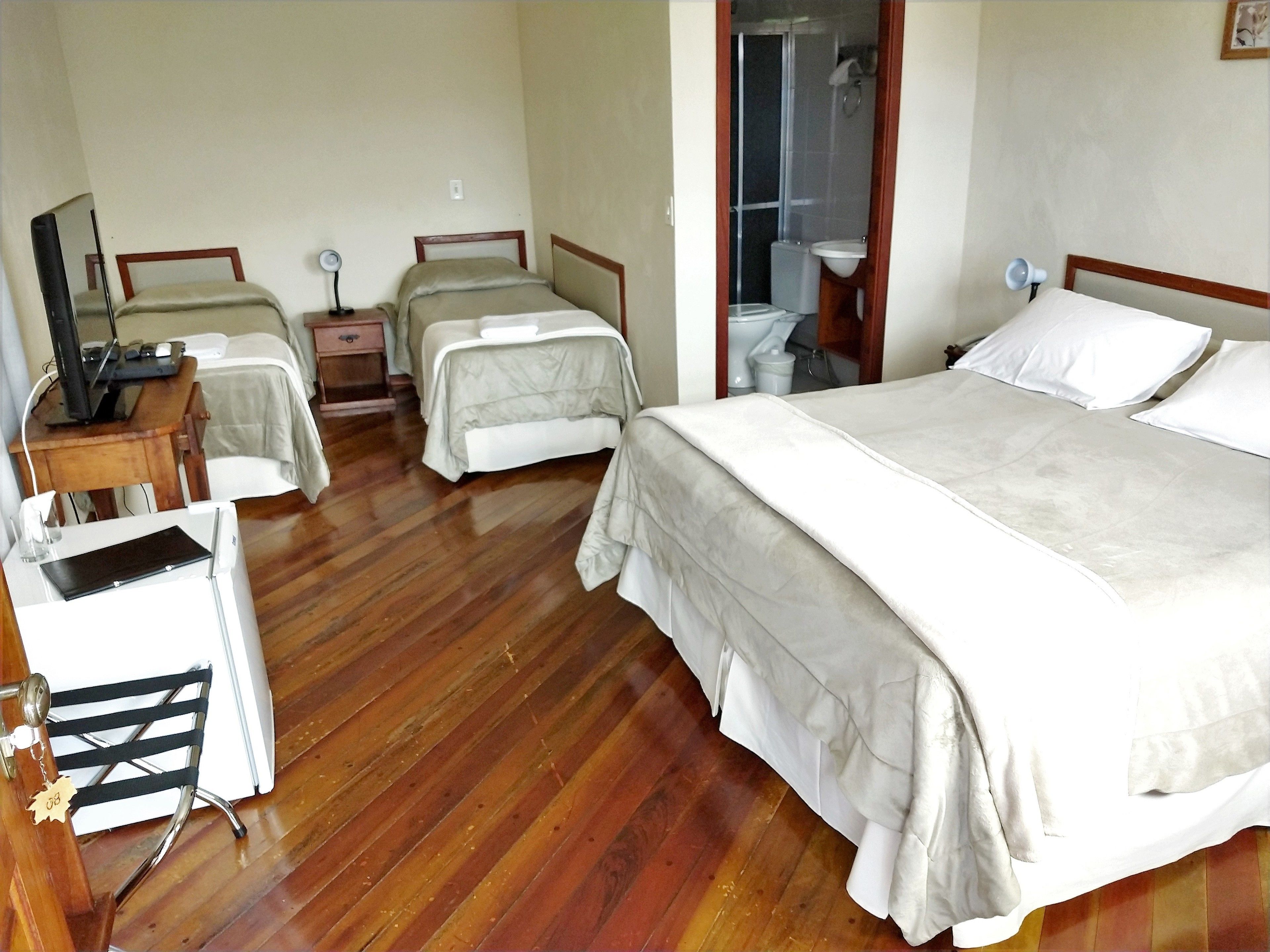 Quarto de hotel com duas camas de solteiro, uma cama maior, uma escrivaninha com computador, uma cadeira e zona de duche.