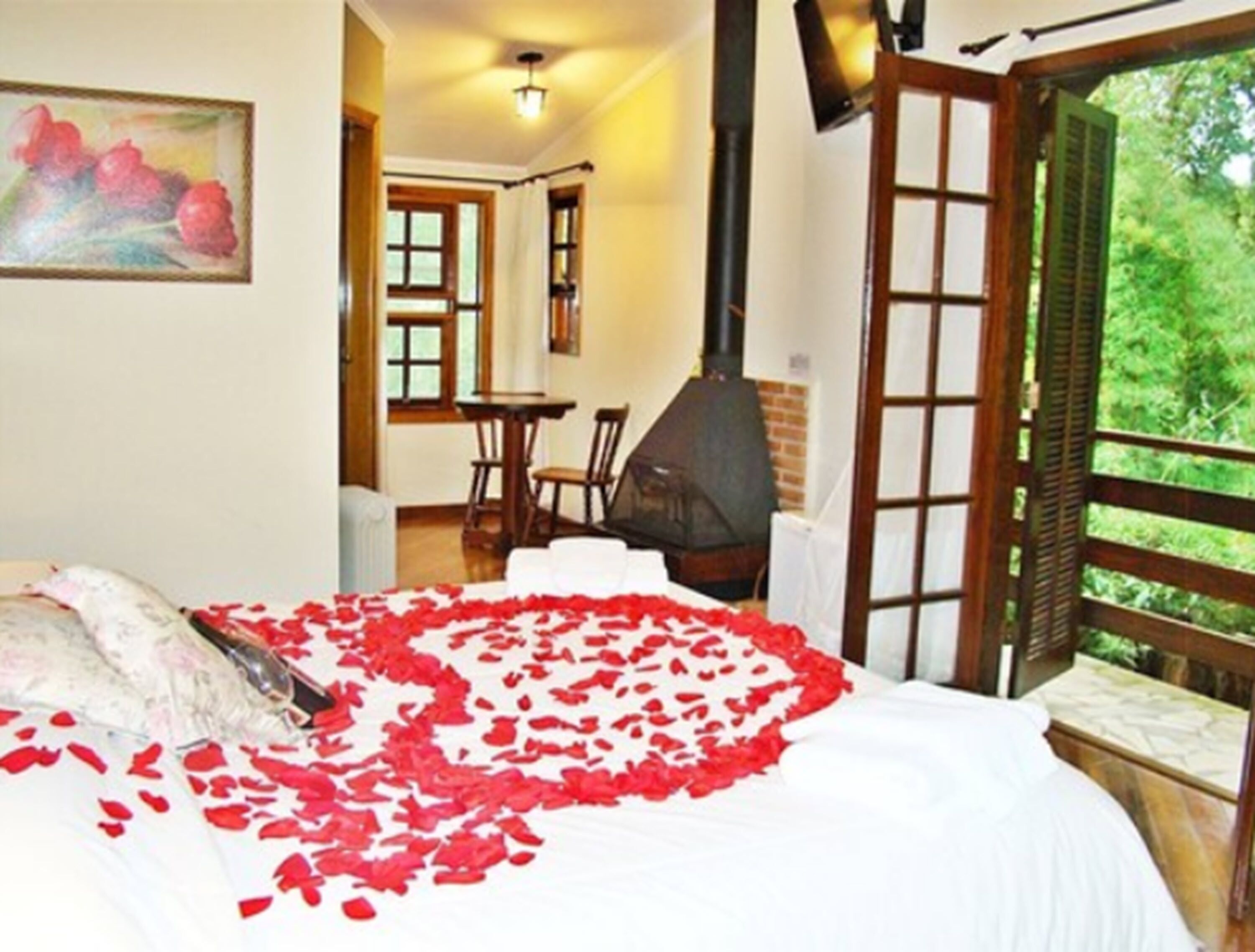 A bedroom with a bed, a painting, a fireplace, and a view of greenery through an open door.