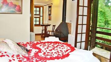 A bedroom with a bed, a painting, a fireplace, and a view of greenery through an open door.