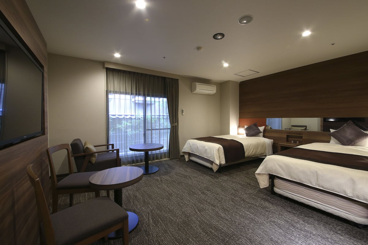 Une chambre d’hôtel avec deux lits, une télévision, un coin salon avec une table et une grande fenêtre.