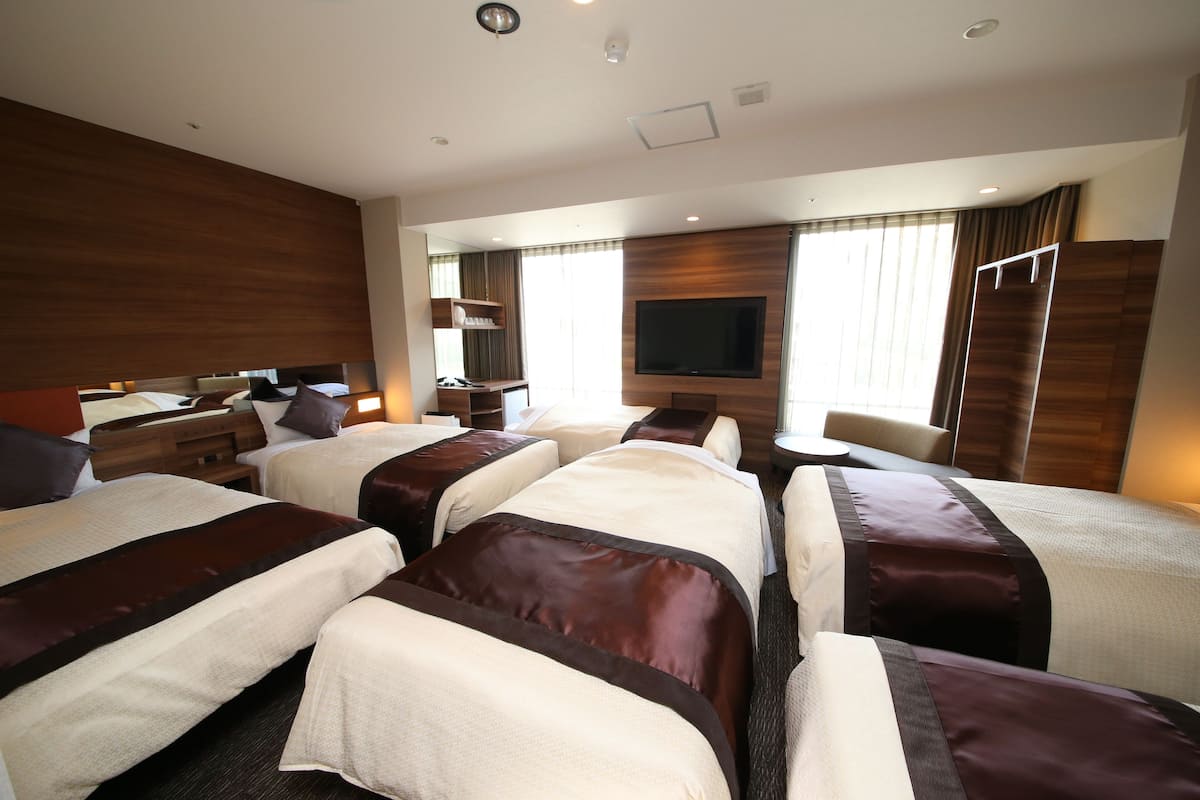 Une chambre d’hôtel avec quatre lits, une télévision, un bureau et une fenêtre avec des rideaux.