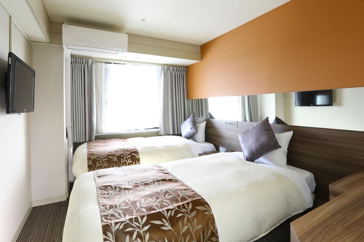 Une chambre d’hôtel avec deux lits, une télévision, un appareil de climatisation et une fenêtre avec des rideaux.