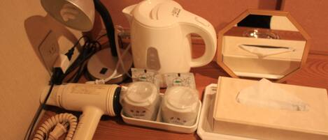A hotel room with a hairdryer, a kettle, a tissue box, and a cup of coffee.