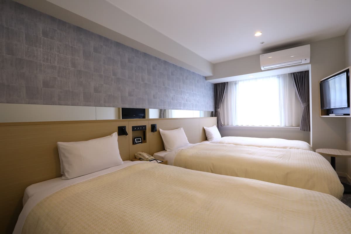 Une chambre d’hôtel avec deux lits, un téléviseur à écran plat, un système de climatisation et une petite table.