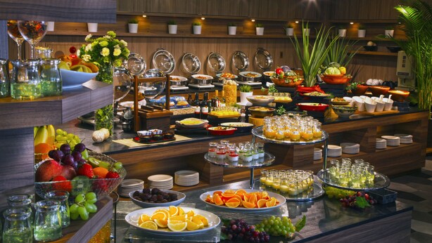 Un bufé con diversas opciones de comida y bebida, entre ellas frutas, verduras y refrescos.