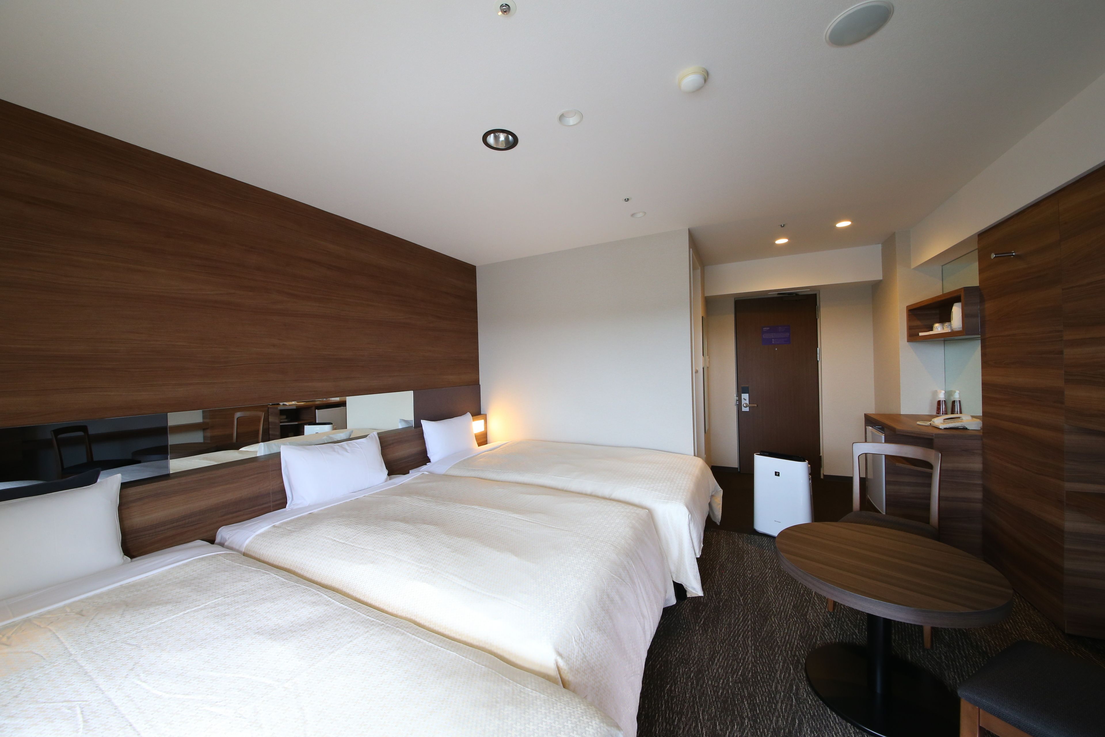 A hotel room with two beds, a small desk, and a chair.