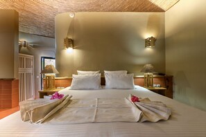 Una cama bien hecha con sábanas y almohadas blancas, una lámpara de noche y una lámpara decorativa en la mesita.