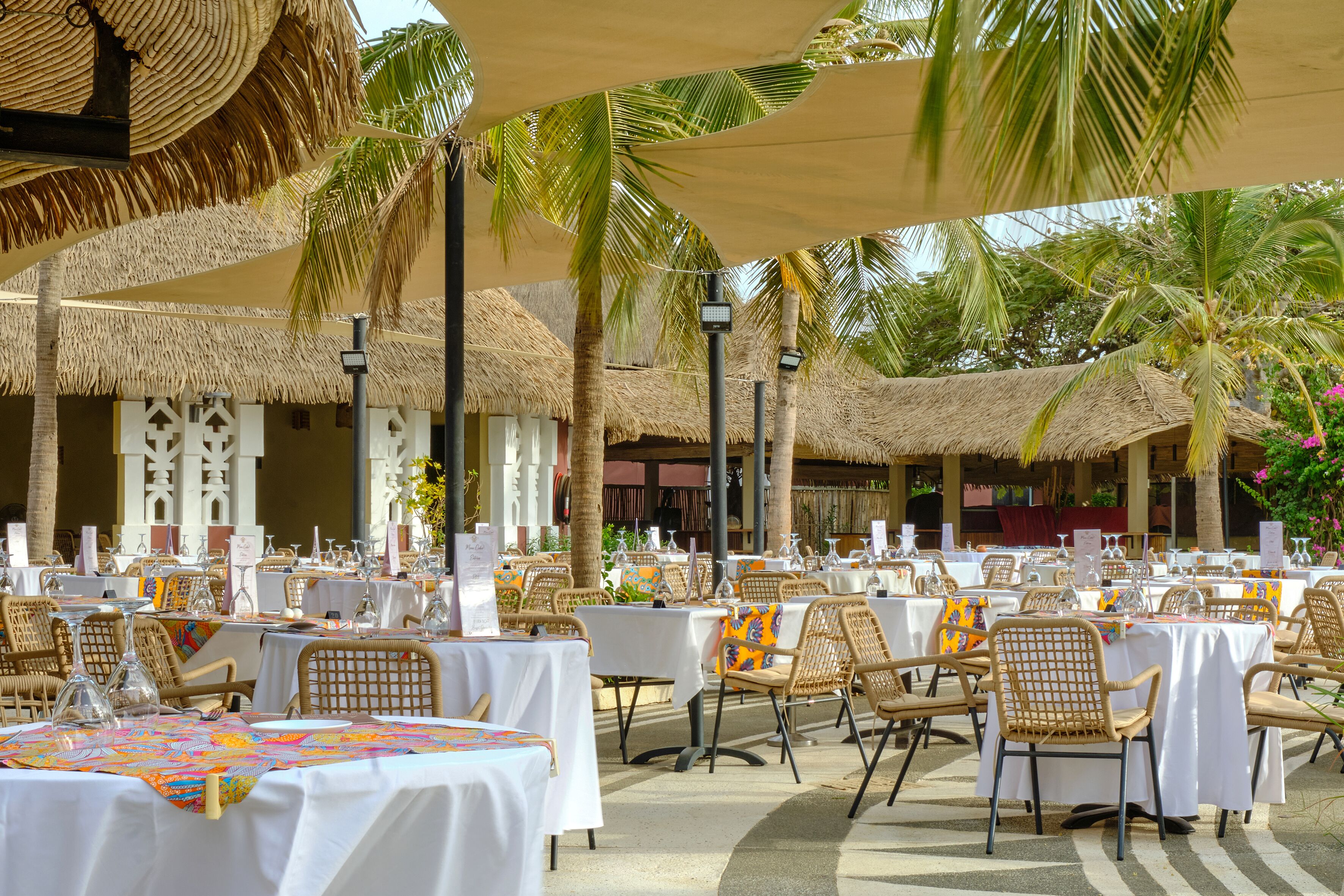 An outdoor dining area with thatched umbrellas, wicker chairs, and white tablecloths.