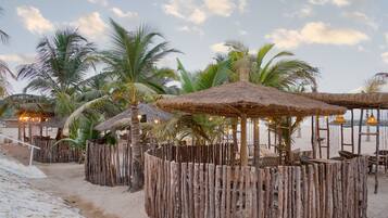 A beachside area with thatched-roof structures, palm trees, and sandy ground.