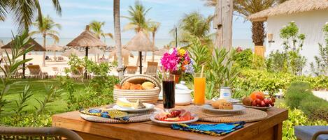An outdoor dining table with breakfast items, a view of the beach, and palm trees.