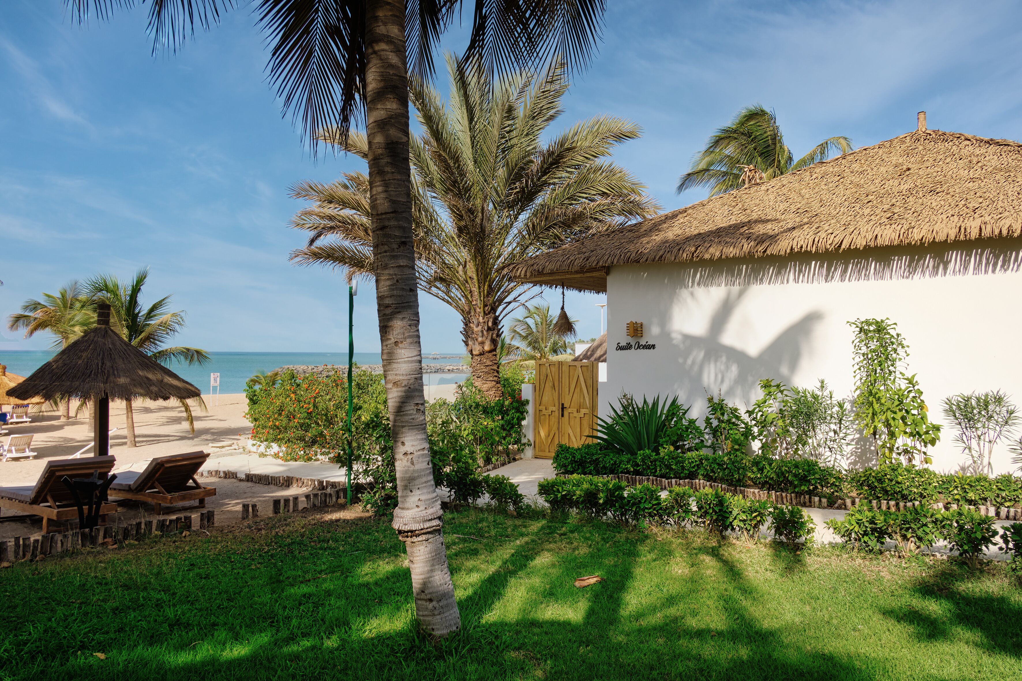 A resort with a thatched-roof building, palm trees, and a beach view.