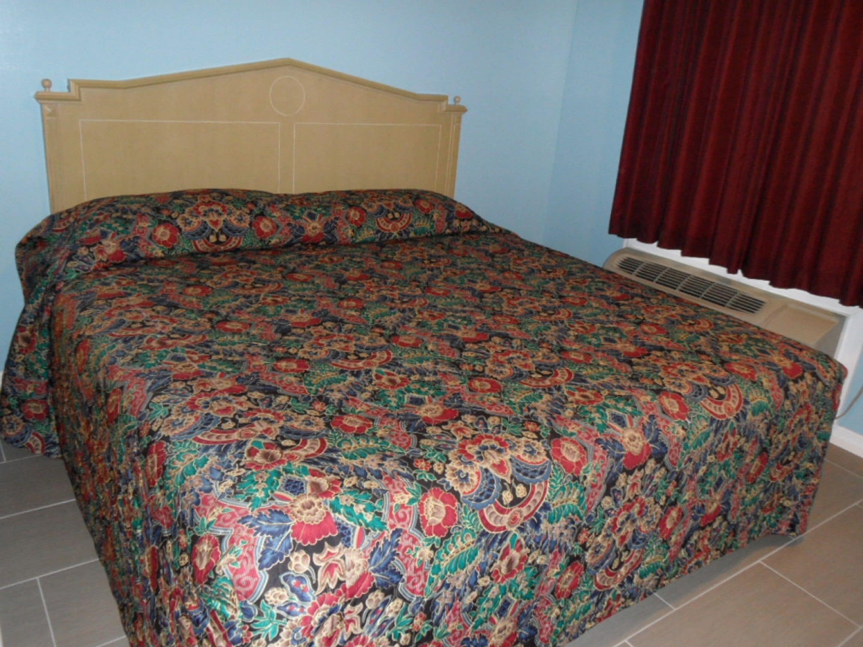 A bed with a patterned bedspread and pillows, a headboard, and a window with curtains.