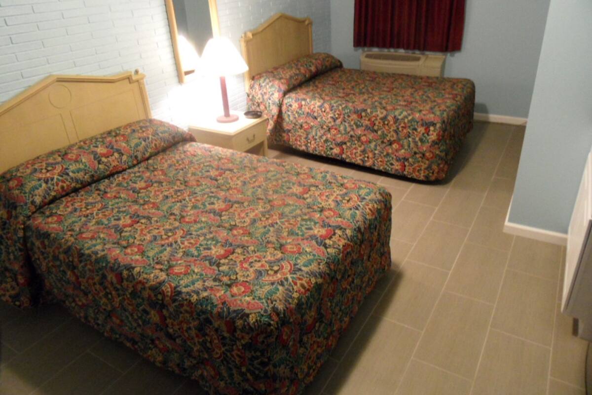 A room with two beds, a nightstand, a mirror, and a window with curtains.
