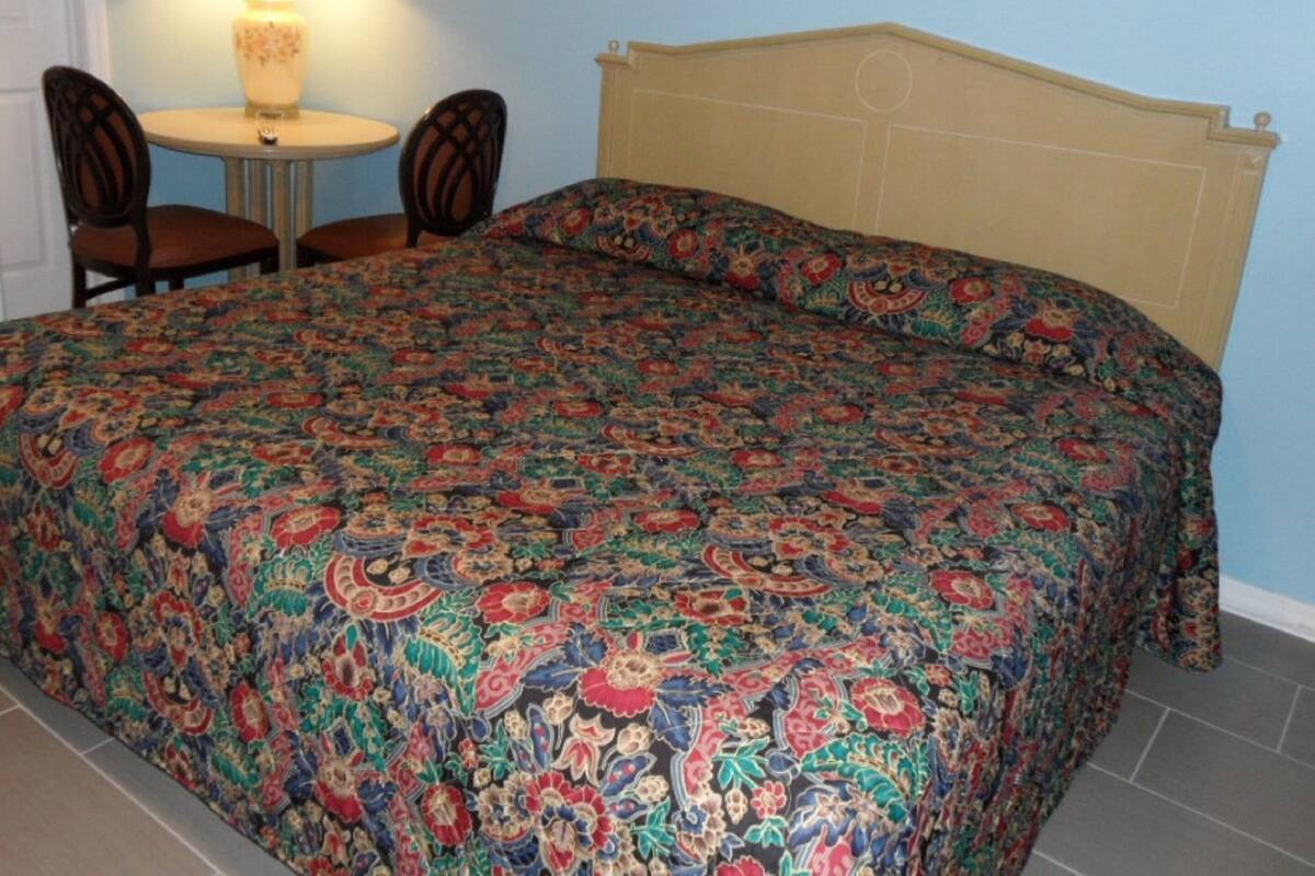 A bed with a patterned bedspread, a bedside table with a lamp, and two chairs.