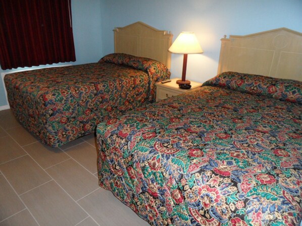 A room with two single beds, a nightstand with a lamp, and a window with curtains.