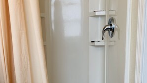 Une petite douche à l’italienne blanche, avec une porte incurvée, un pommeau de douche et un drain.
