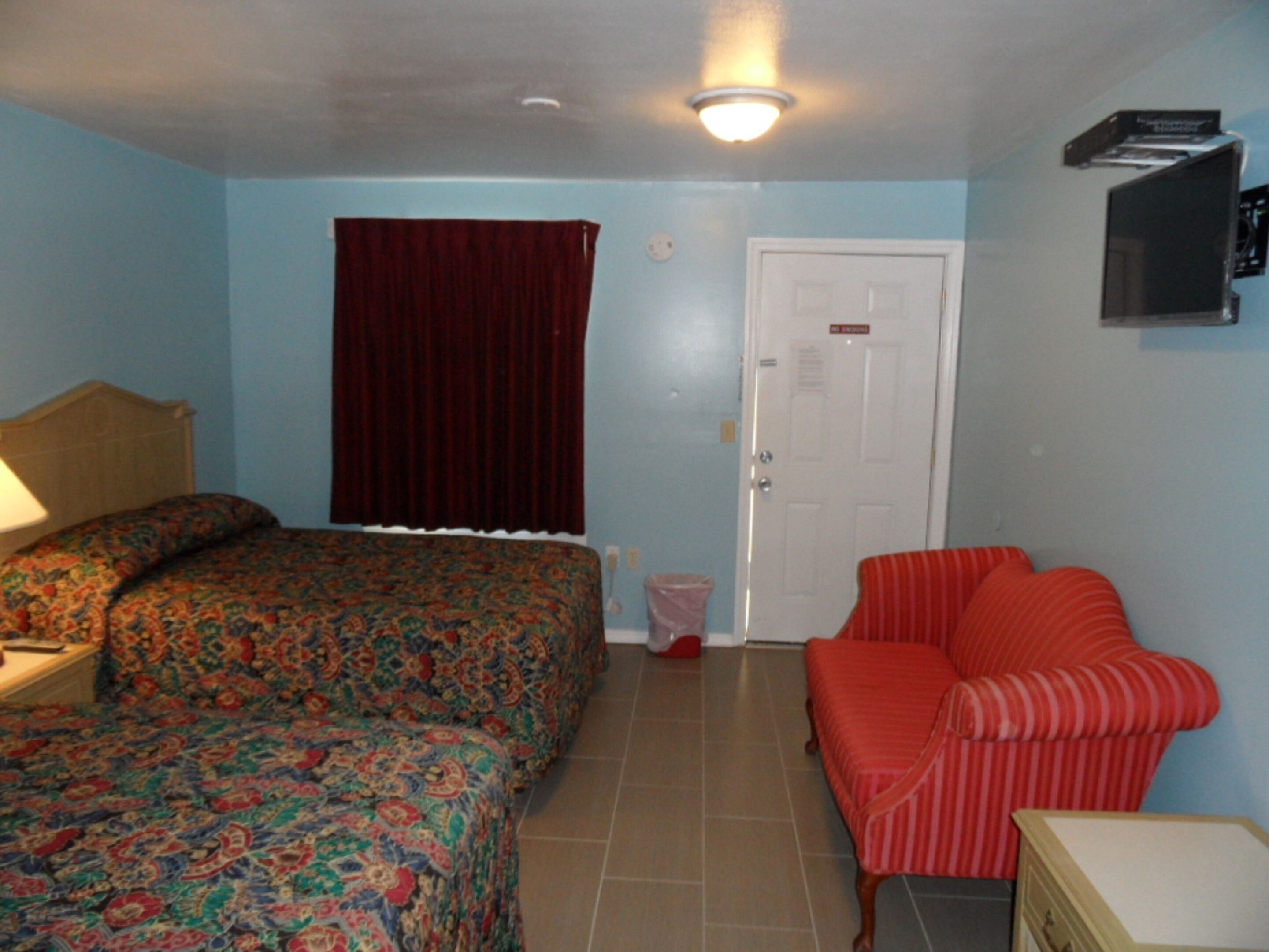 A bedroom with a bed, a chair, a nightstand, a door, and a ceiling light.