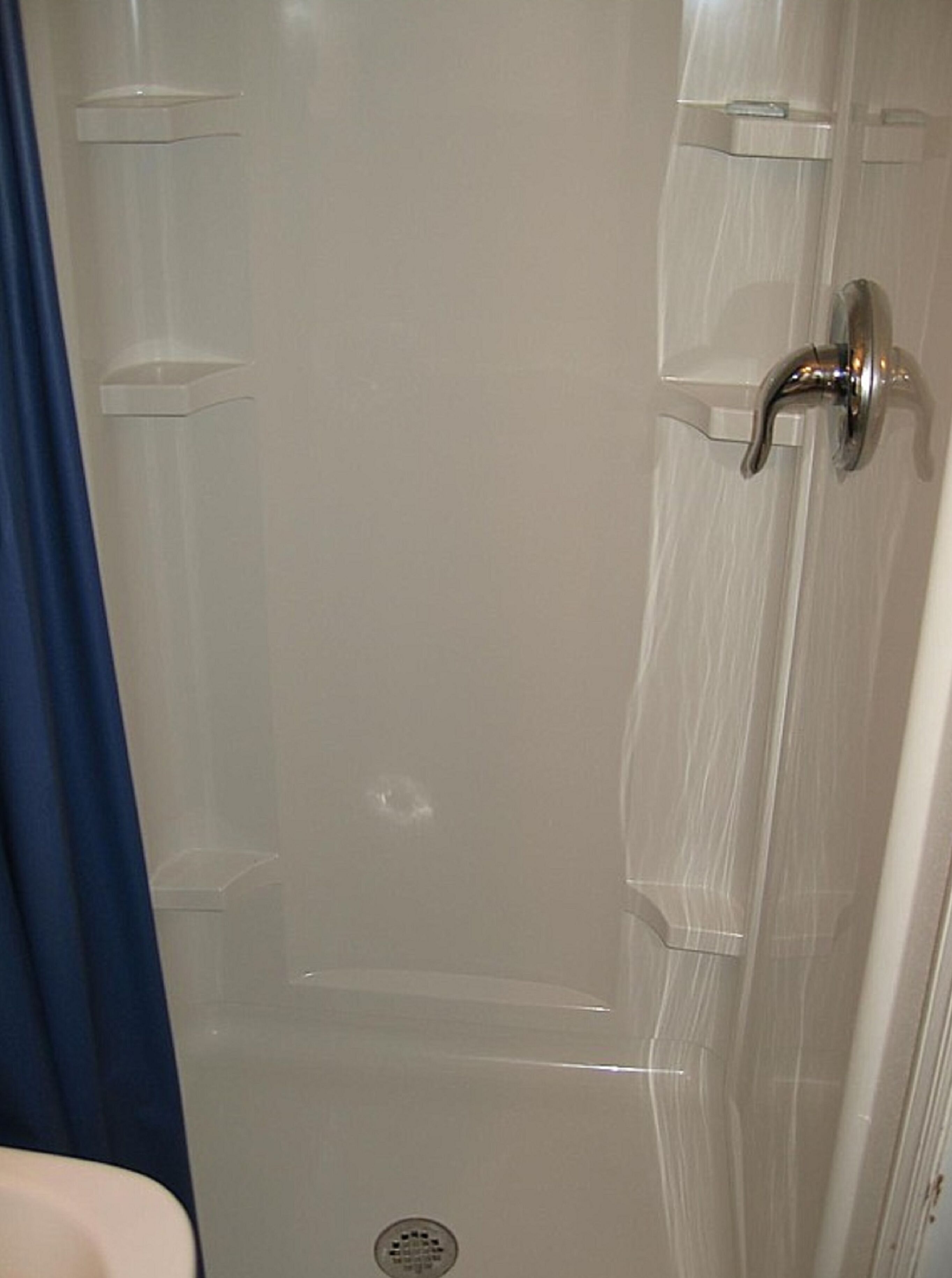 A bathroom with a white door, a shower curtain, and a visible drain.