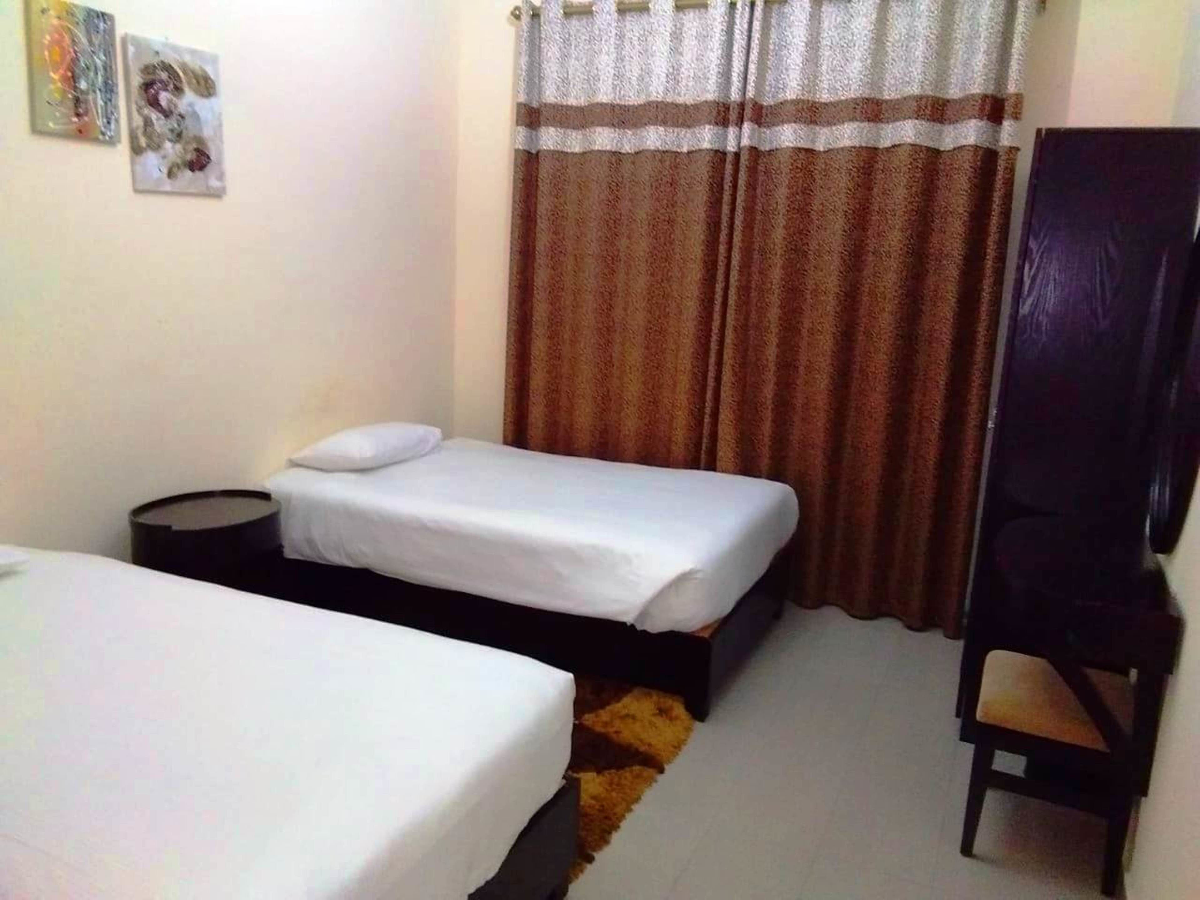 A small, simple room with two single beds, a chair, and a small table.
