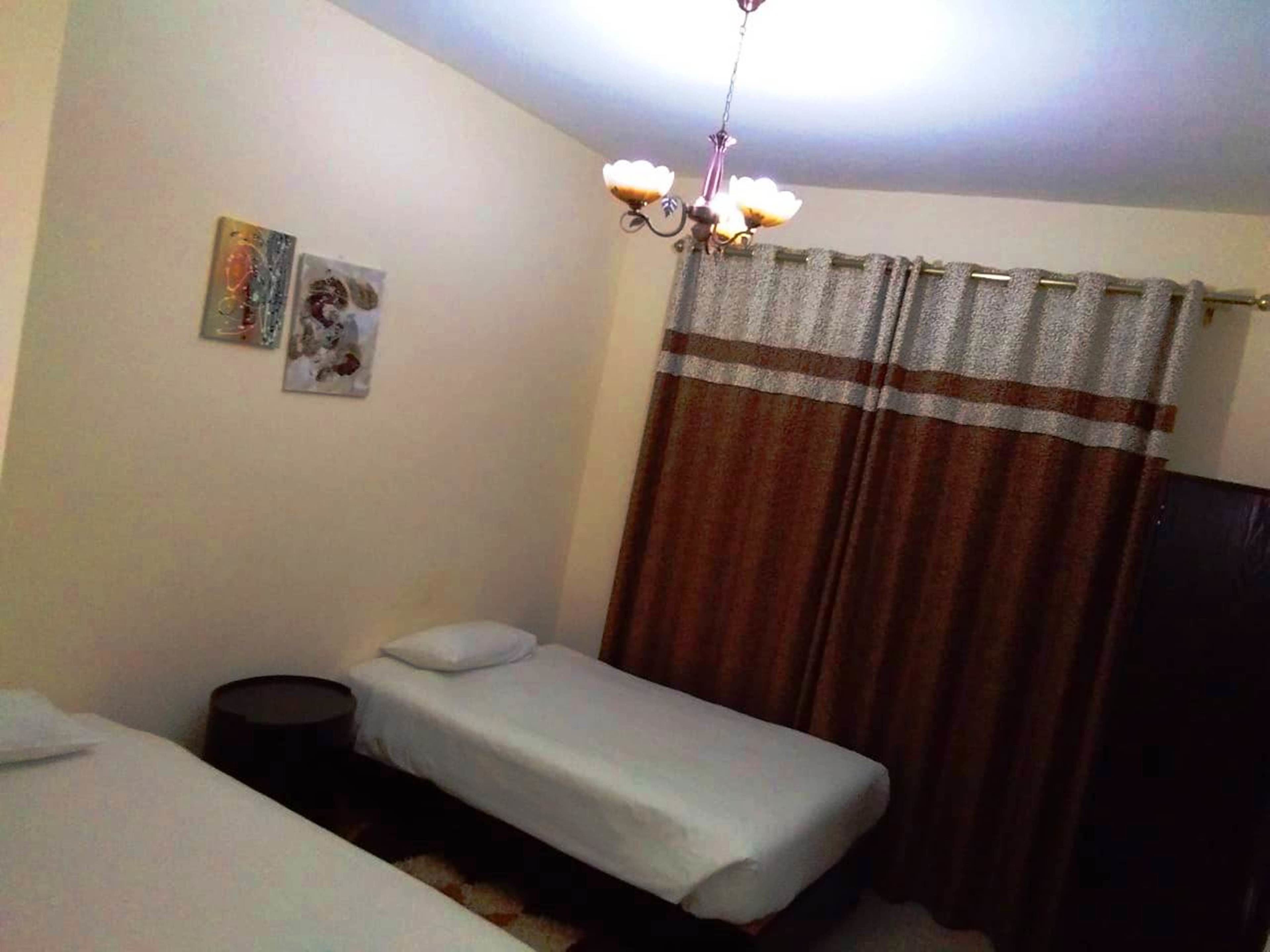 A small, simple room with two single beds, a small table, and a curtain.