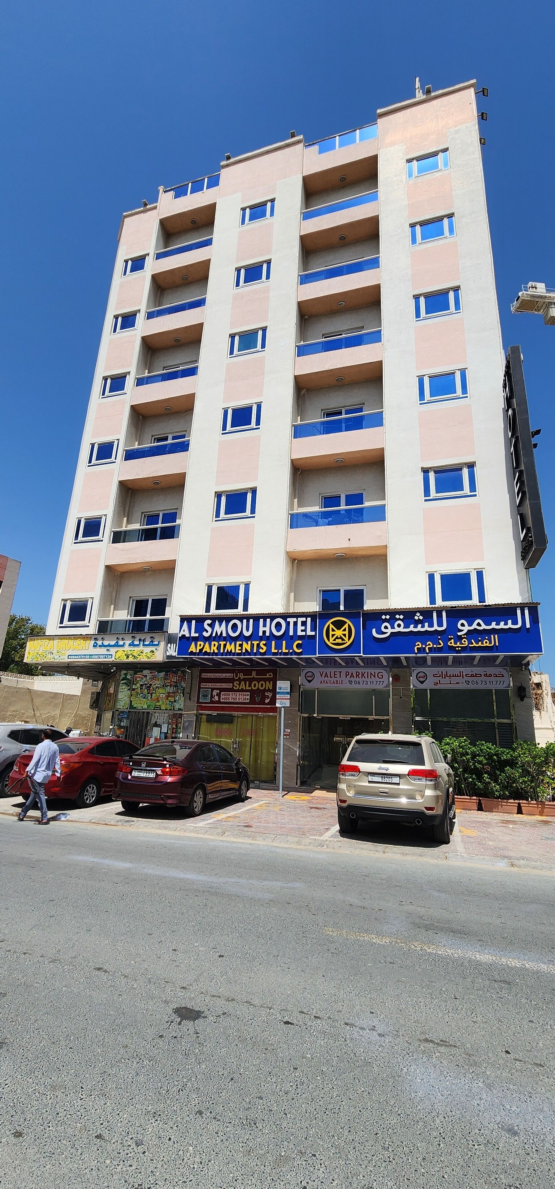 Un hotel de varios pisos con balcones, un área de estacionamiento y un escaparate con señalización en árabe.