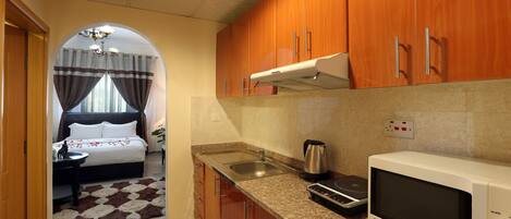 A compact kitchen with wooden cabinets, a microwave, a kettle, and a sink.