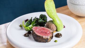 A plate with a slice of meat, broccoli, and a green vegetable.
