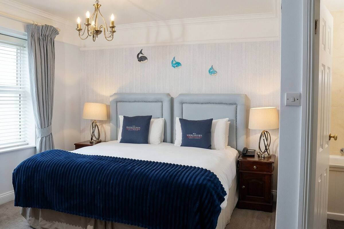 A bedroom with a bed, two bedside tables, a chandelier, a window with curtains, and wall-mounted decor.