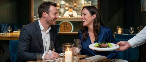 A couple dining at a restaurant with a wooden table, candles, and a menu.