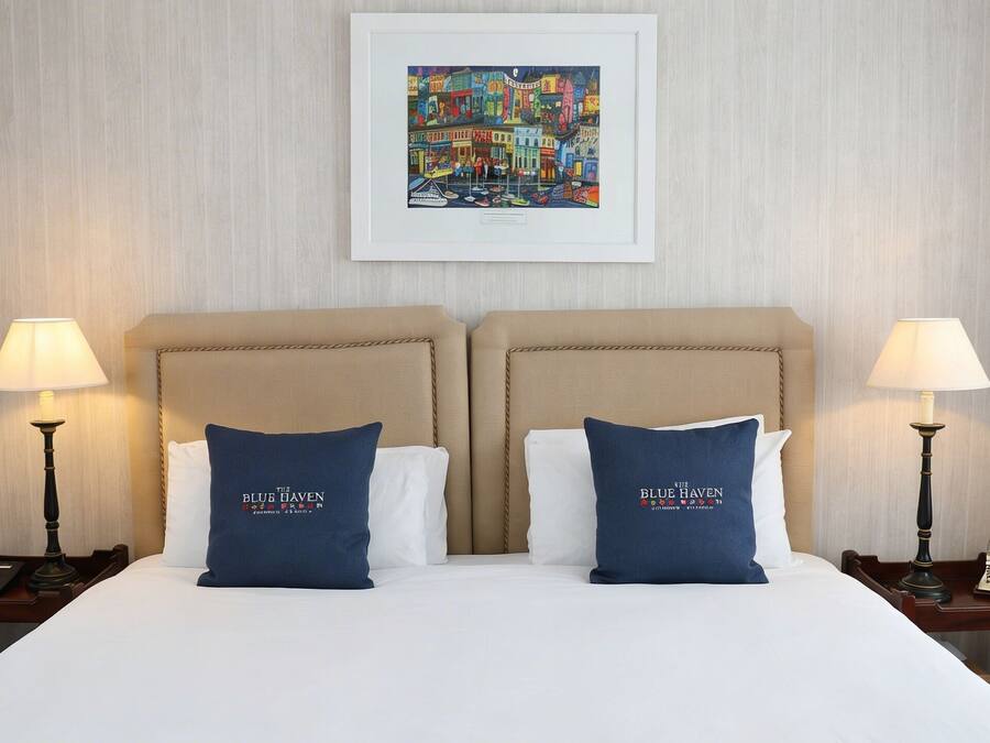 A hotel room with a bed, two bedside lamps, two nightstands, and a framed artwork on the wall.
