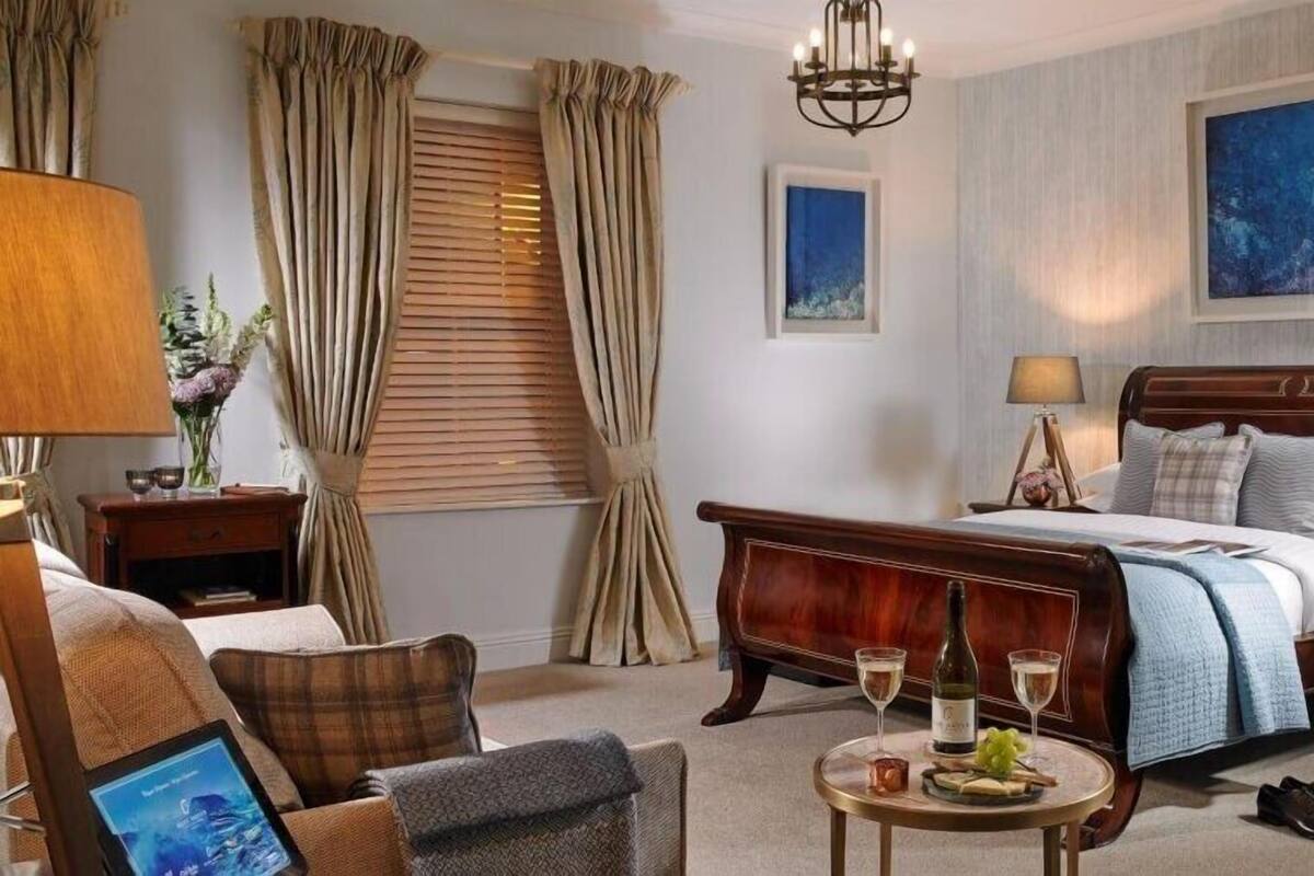 A hotel room with a large bed, a desk, a chair, a round table with drinks, and curtains.