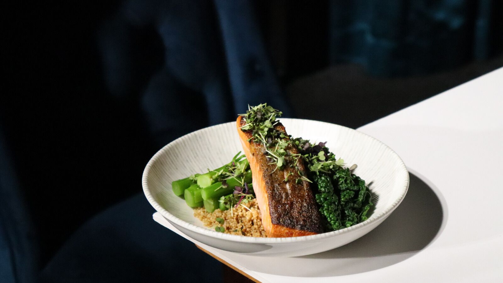 A white plate with a piece of grilled fish, green vegetables, and grains.