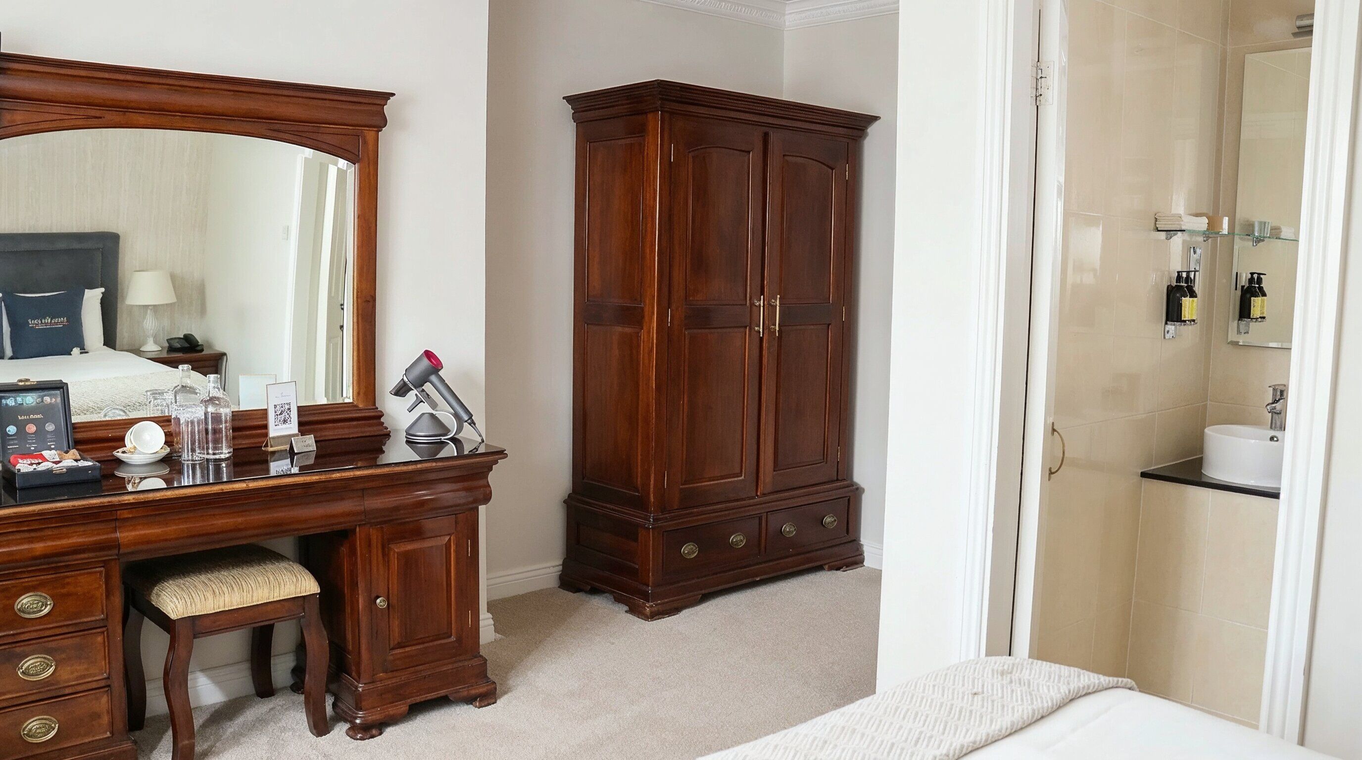 Une chambre d’hôtel avec une commode en bois, un miroir, une coiffeuse avec des articles de toilette, un lit et un dressing.