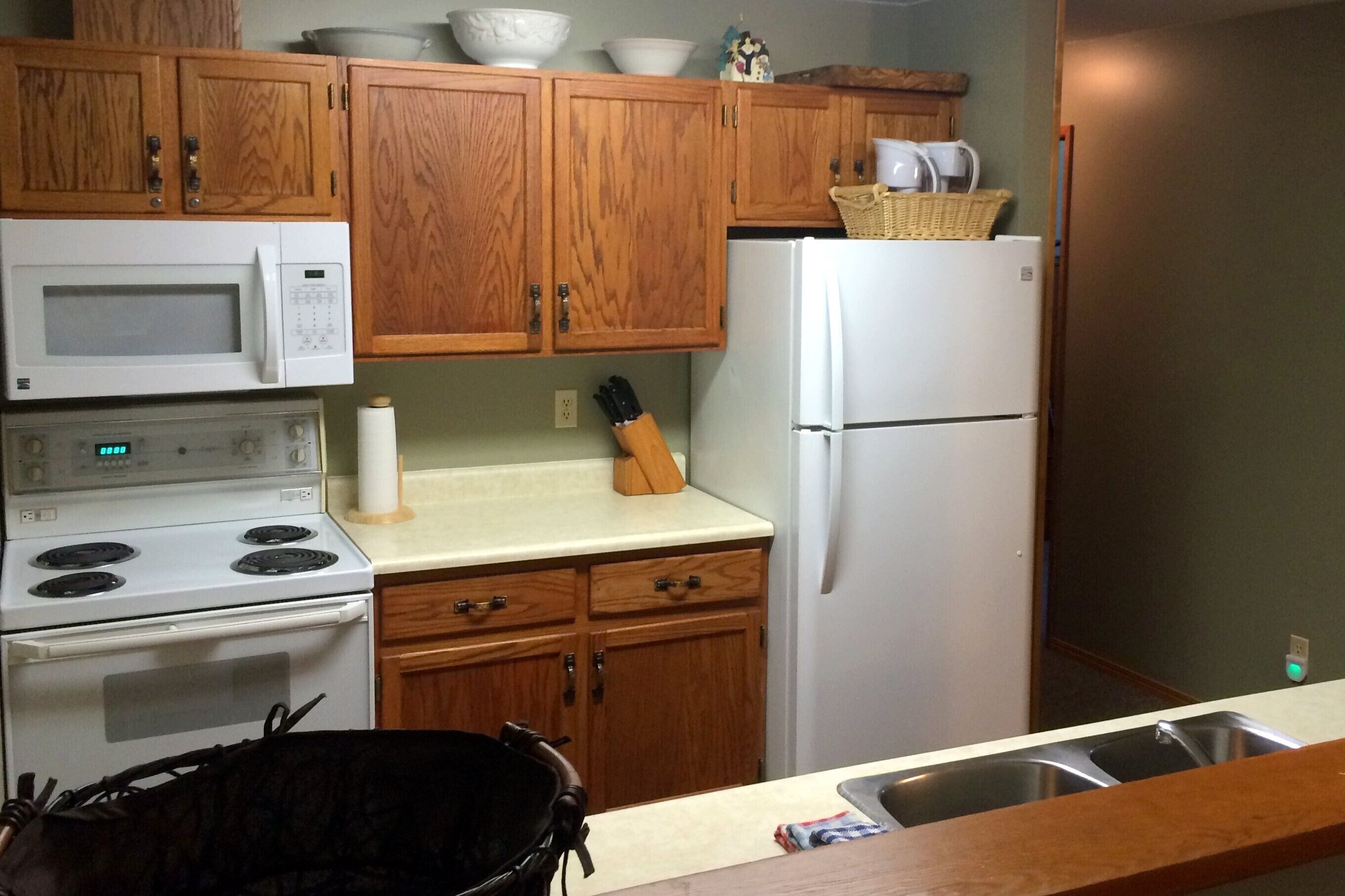 Una cocina con armarios de madera, una estufa blanca, un microondas, un refrigerador y un lavamanos.
