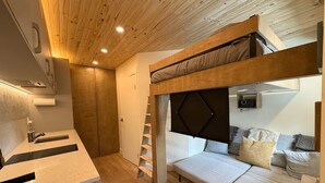 Une pièce compacte comprenant un lit superposé, un coin cuisine et un petit espace salon.