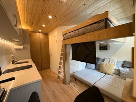 Una habitación pequeña con literas, kitchenette y un espacio de descanso.