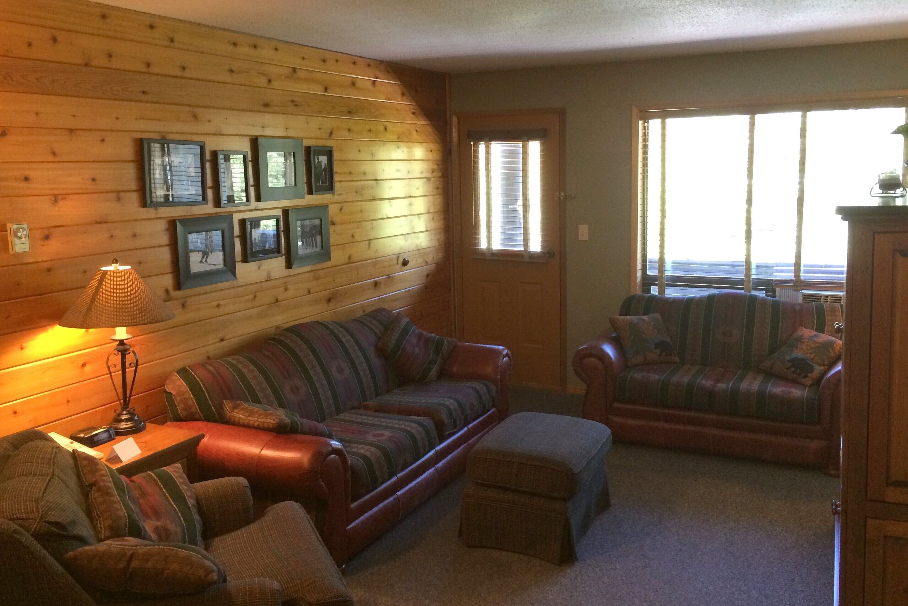 A cozy living room with a wooden wall, a sofa, a loveseat, and a lamp.