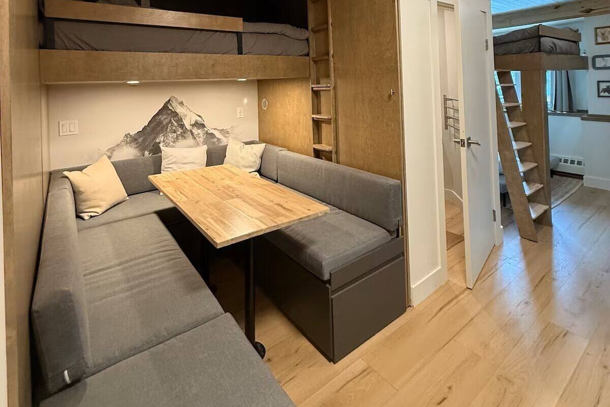 Un espace de vie compact comprenant un lit en mezzanine, un canapé, une petite table et un escalier menant à un niveau supérieur.