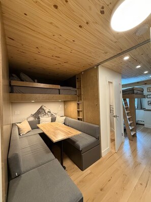 A compact living space with a loft bed, a sofa, a small table, and a staircase leading to an upper level. - The Griz Inn (Fernie)