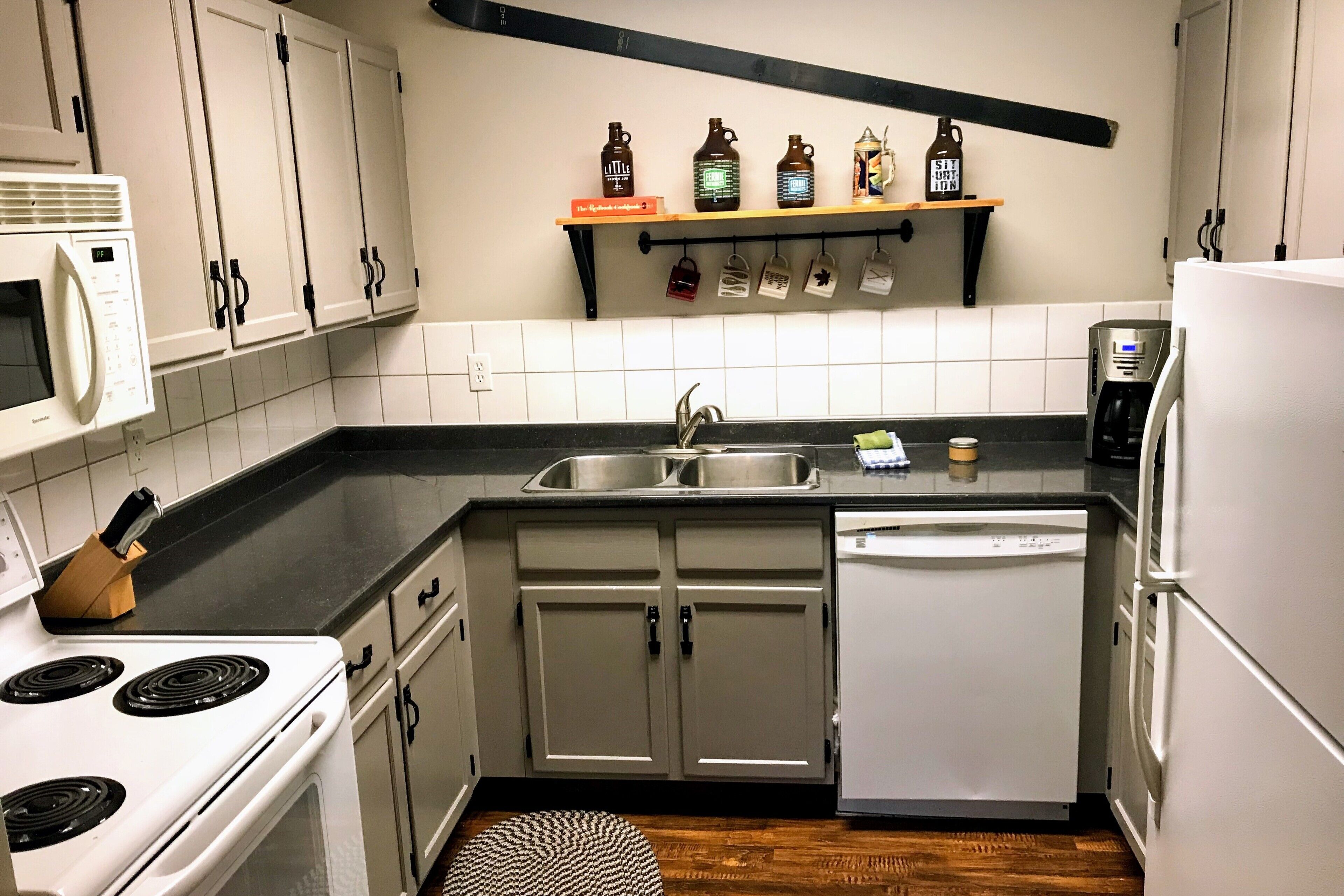 Una cocina compacta con armarios blancos, microondas, estufa, lavavajillas y cafetera.