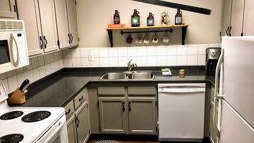 Una cocina compacta con armarios blancos, microondas, estufa, lavavajillas y cafetera.