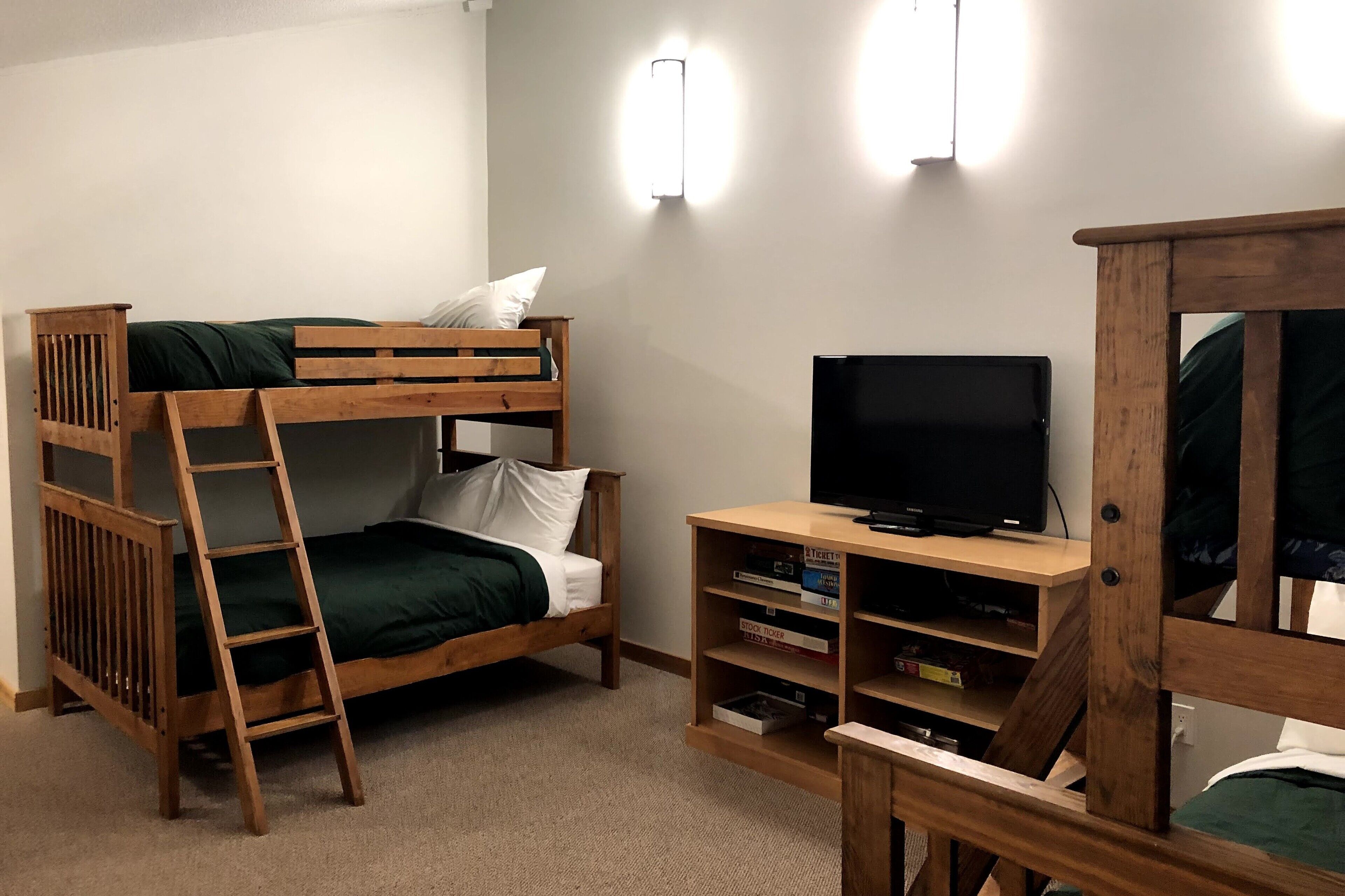 Una cama litera con escalera, un televisor sobre un soporte de madera y una estantería con libros.